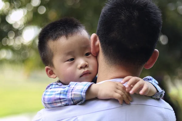 Chinese little boy hugging his father. The boy looks thoughtfully to one side.