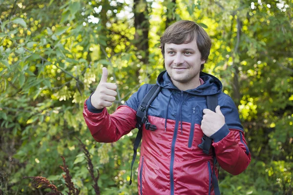 The guy with the backpack hiking in the forest. Young man showing thumb up