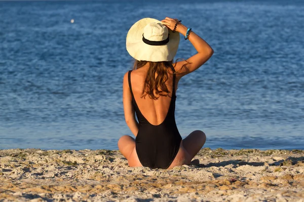 Blonde girl in panama, sitting on the beach, looking  sea. Summer photo