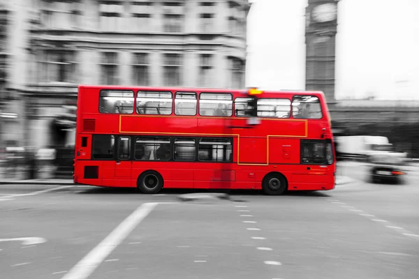 Red London Bus in motion blur surrounded by the black and white city of London