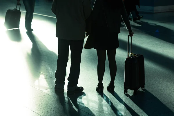 Traveling people with trolley bags at the airport in backlit