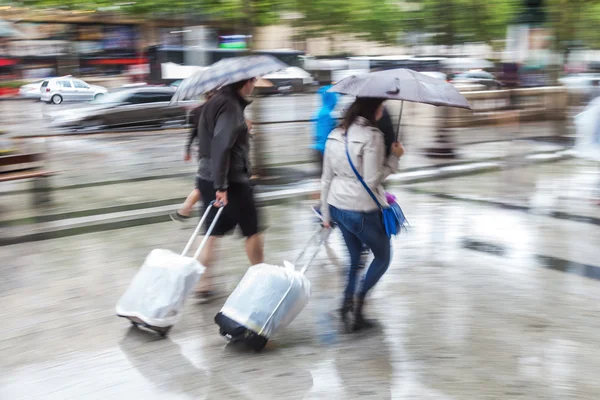 Women with trolleys and rain umbrellas walking in the rainy city