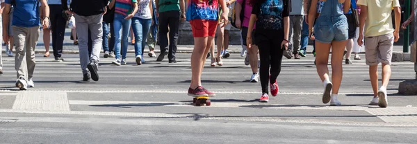 Crowd of people and a skateboarder crossing a street