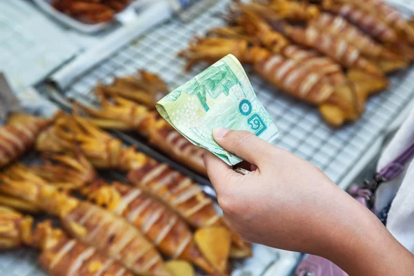 Hand with Thai Baht paying at a cookshop in Bangkok, Thailand