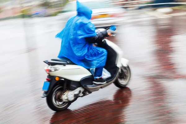 Scooterist with rain cape in motion blur