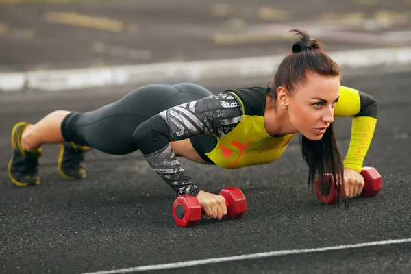 Fitness woman doing push-ups in the stadium, cross training workout. Sporty girl training outside