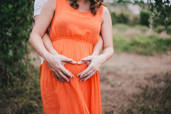 Young pregnant woman with her husband holding hands on her belly