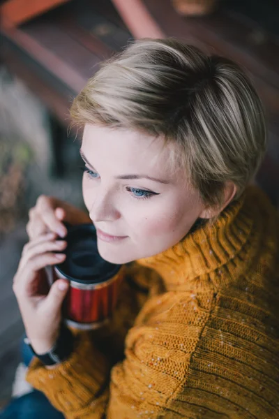 Blond with blue eyes sitting near lake with cup of hot tea