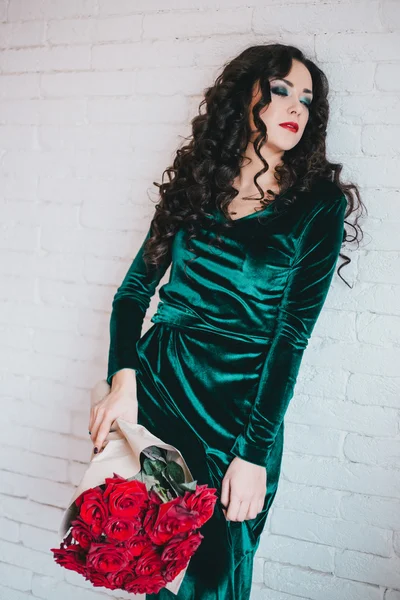 Beautiful woman in a green dress and red shoes with red roses