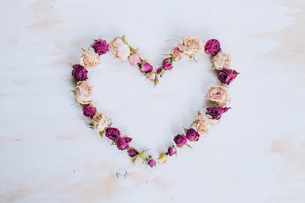 Dry rose flowers in heart shape on old wooden background