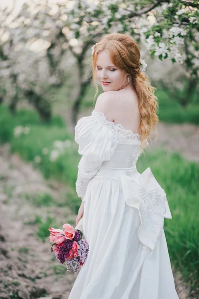 Beautiful bride in a vintage wedding dress posing in a blooming apple garden