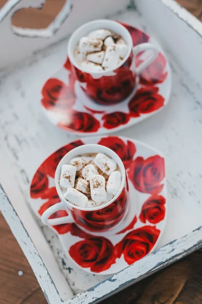 Two cups of hot cocoa with marshmallows and cinnamon on wooden background