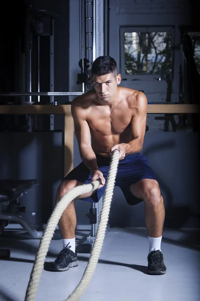Muscular man in gym with battle ropes