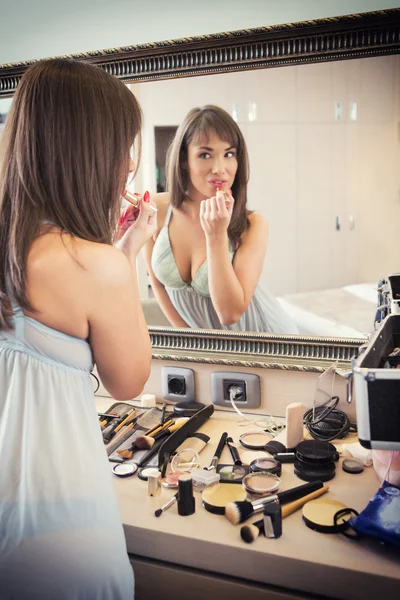 Cheerful young woman in front of mirror applying make-up