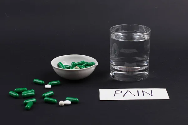 Pills with glass of water to drink the pills on dark black background. Pain