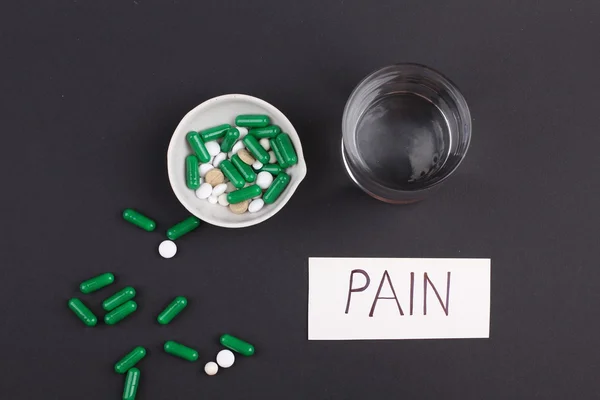 Pills with glass of water to drink the pills on dark black background. Pain