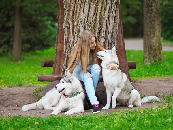Attractive young woman sits on the bench with two funny siberian husky dogs