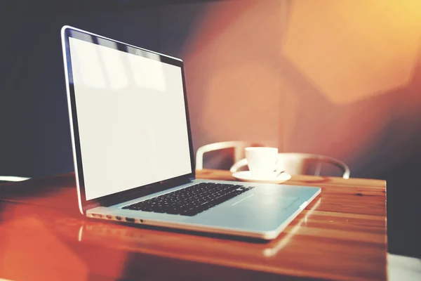 Open laptop computer and cup of coffee lying on wooden table in cafe bar interior