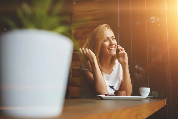 Smiling woman calling with mobile phone during morning breakfast in cafe
