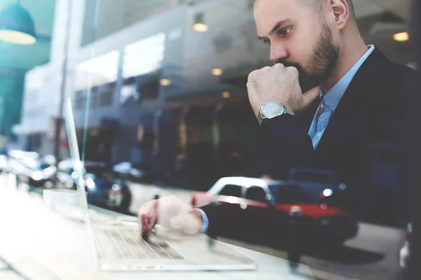 Serious male CEO is working on laptop computer, while is sitting in urban coffee shop of New York city.