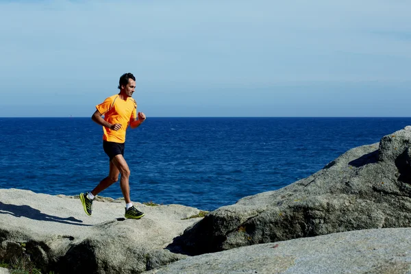 Male jogger in fluorescent t-shirt runs over sea rocks