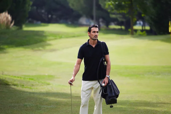 Attractive male golf player at the course with a club sack