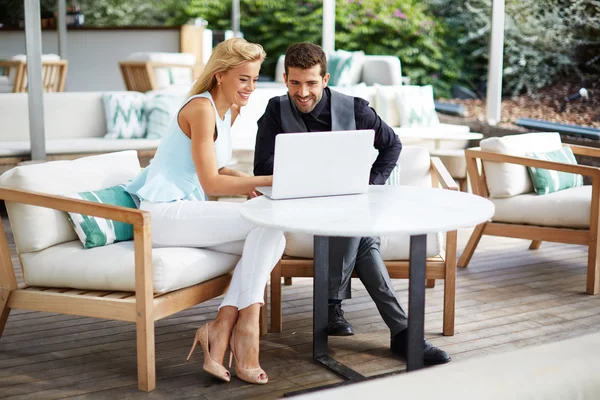 Business team of two successful people sitting outdoors in lounge terrace and planning work, businessman and businesswoman meeting in modern cafe, business partners having working with computer
