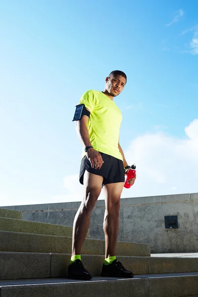 Dark skinned athletic runner with muscular strong body resting after jogging, beautiful fit man in bright fluorescent sportswear, sports fitness concept