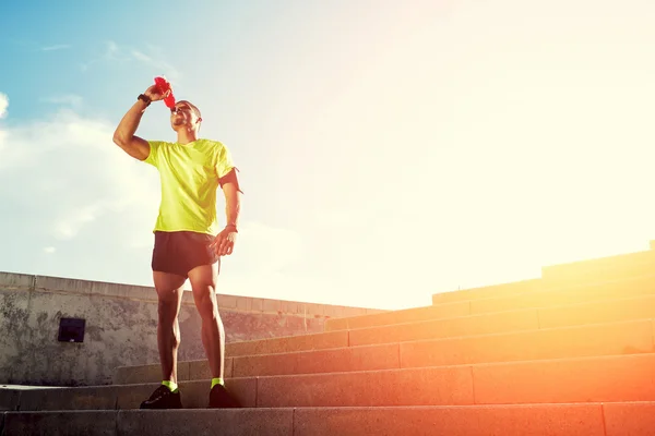 Dark-skinned runner drink water after intensive evening run, beautiful fit man in bright fluorescent sportswear, sports fitness concept