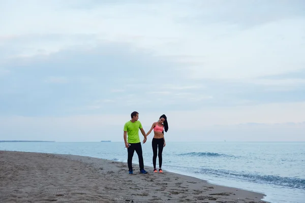 Sport couple walking along the beach resting after workout, sexy fit woman and man dressed in fluorescent-shirt taking break after run, couple of runners resting after fitness training outdoors