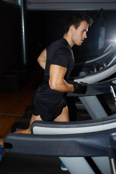 Handsome brunette man at workout in gym running fast on a treadmill, fit man running in a gym on a treadmill looking to the screen, attractive sportsman at the gym doing exercise on the treadmill