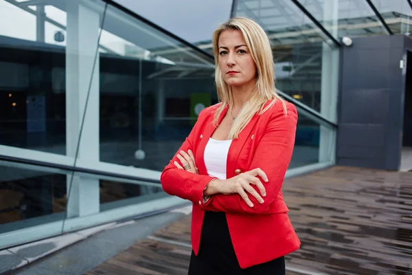 Portrait of a confident businesswoman standing against skyscraper office building, professional businesswoman with arms crossed, successful business woman looking confident