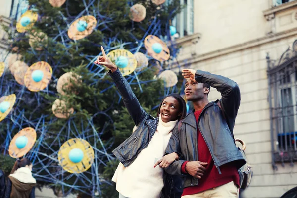 Charming woman pointing with he finger something interesting, romantic couple walk on christmas tree background on big square, laughing couple on christmas vacation walking in the city