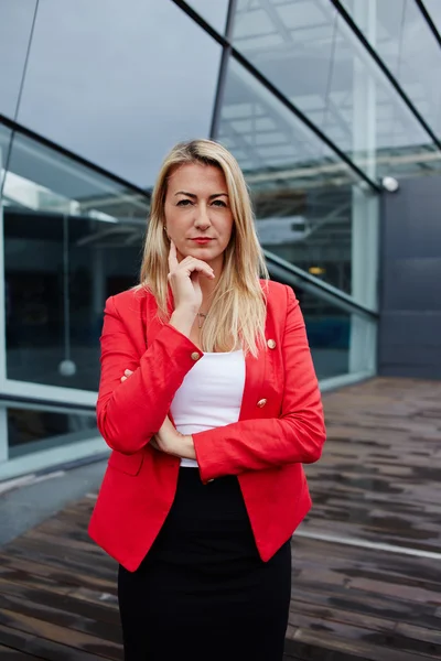 Portrait of confident young businesswoman in suit reflectively looking to the camera, executive woman carefully listen to the employee, confident business woman in red jacket standing near office