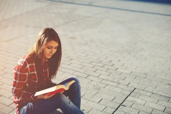 Beautiful girl has a rest sitting on the ground with a book in their hands