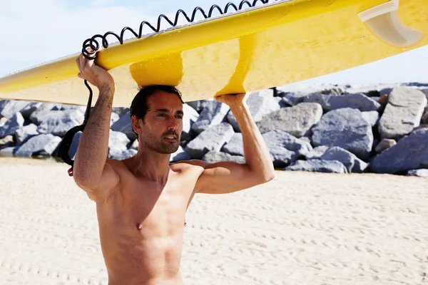 Brunette man carrying big surfboard