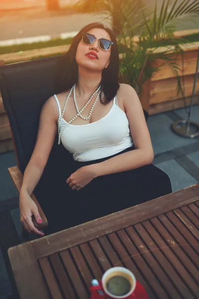 Woman in fashionable sunglasses sitting in cafe