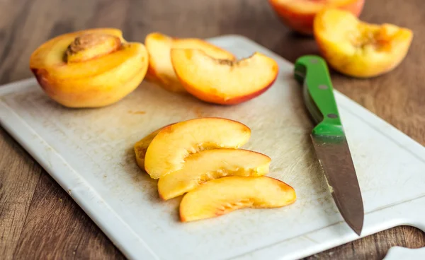 Cut slices of ripe peach on a white board, green knife