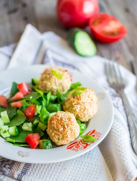 Baked chickpeas balls with sesame and vegetable salad on a gray