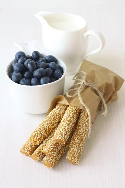 sesame sticks, blueberries and milk on white background