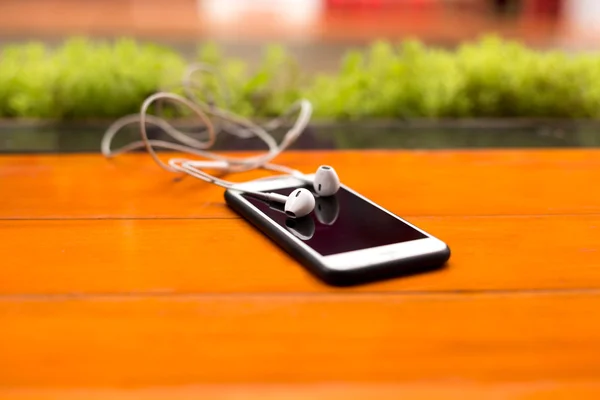 Empty screen of cell phone and eare phone on wooden table