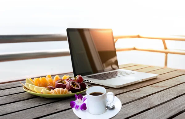 Fruits salad and cup of coffee and flower with computer laptop