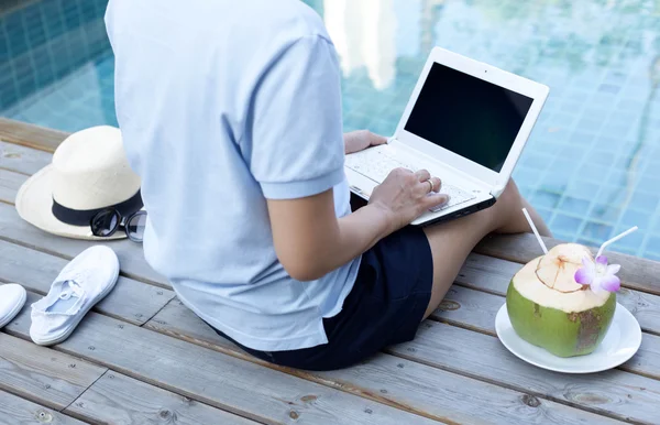 Women using a laptop computer by swimming pool