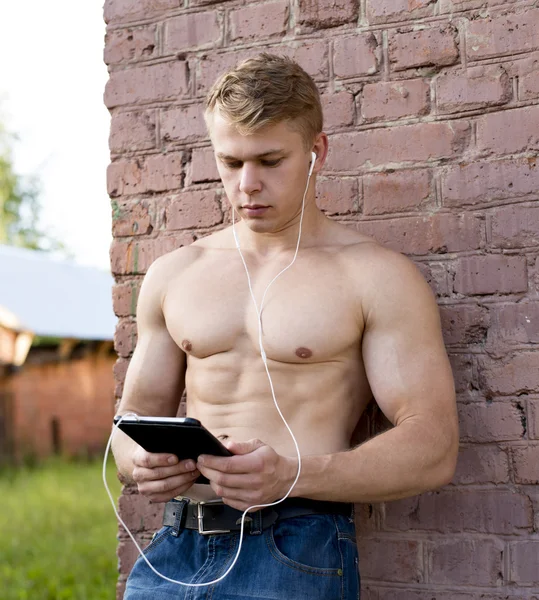 Young bodybuilder man is resting on nature of the tablet in hands and watching movie