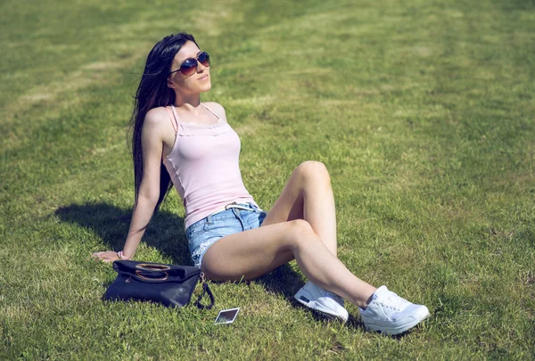 Beautiful young girl sunbathe on the grass, relaxing after work, throwing phone and bag aside,