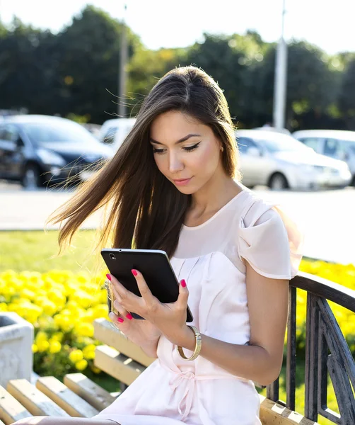 Beautiful girl holding a tablet,  bright sunny day, on  bench, fashion style urban life. Read e-books, sitting  social networks, watching  movie  your