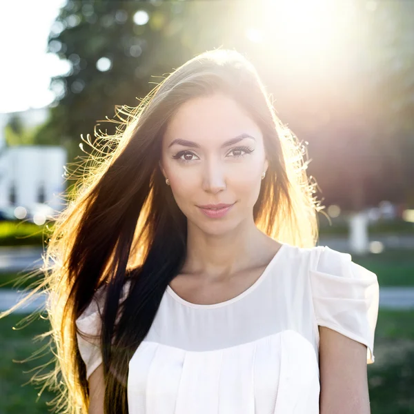 Portrait of a beautiful brunette in  park in bright sunlight. Fashion style  urban life, emotionally looks. Outdoor summer.