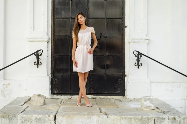 Beautiful brunette girl in a black metal door on the stairs poses. Fashion style. Tanned woman in pink dress outdoors resting against the background of the concept  the Church