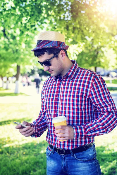 Man in  shirt and jeans  sunglasses, holding  mobile phone coffee or tea, read the conversation messages on your , the concept of summer,  businessman  vacation. City lifestyle.  the street in the