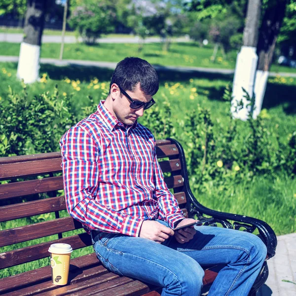 Man in  shirt and jeans  sunglasses, video looks on the tablet corresponds to the social networks, in the summer  the bench, the concept of  businessman  vacation. City lifestyle.  the street in the